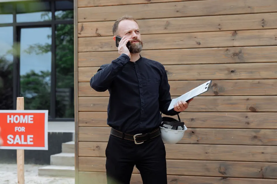 A real estate agent on a phone call outside a house, holding documents