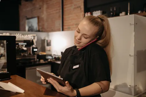 A café worker on the phone while checking a tablet at the counter