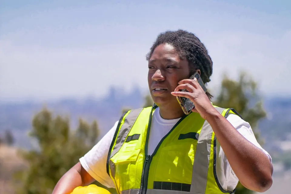 A construction worker in safety gear talking on a phone outdoors
