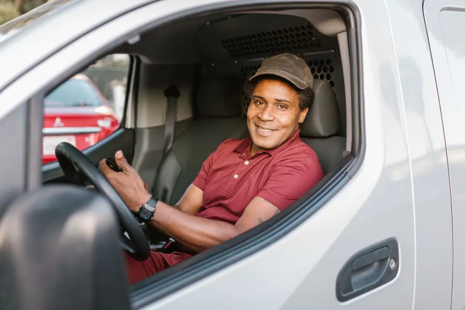 A smiling tradesperson in his van holding a phone