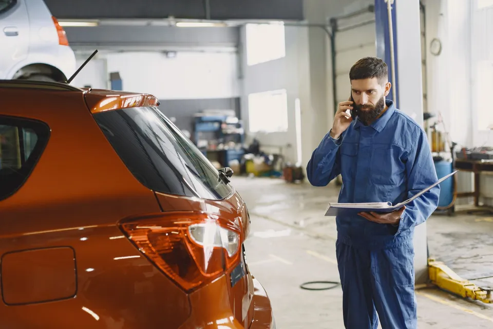 A mechanic on a phone call beside a car in an auto repair shop